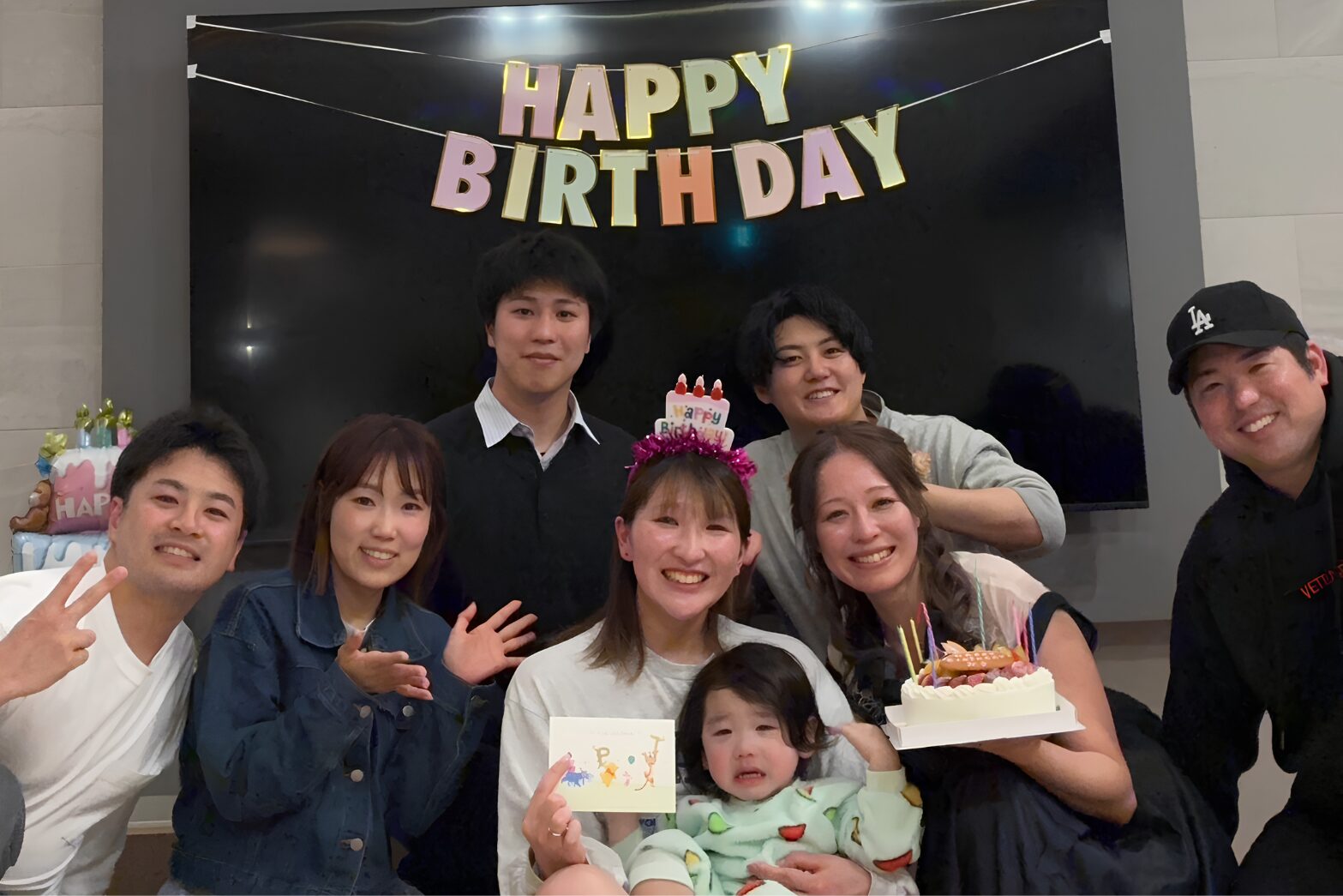 誕生日パーティーで家族や友人が笑顔で集まり、主役を囲んで記念撮影をしている様子。人生の支えとなる仲間や家族との絆をイメージしたアイキャッチ画像。